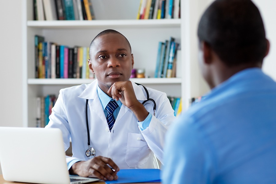 African american doctor listening to problems of male patient at hospital